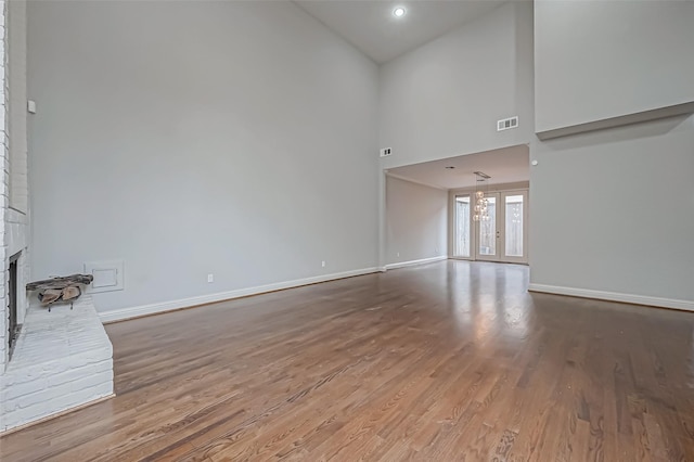 unfurnished living room with a high ceiling, wood finished floors, visible vents, baseboards, and a brick fireplace