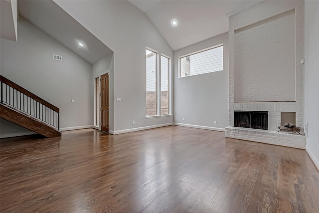 unfurnished living room featuring baseboards, visible vents, wood finished floors, a fireplace, and high vaulted ceiling