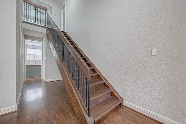 stairway featuring a textured wall, wood finished floors, a towering ceiling, and baseboards