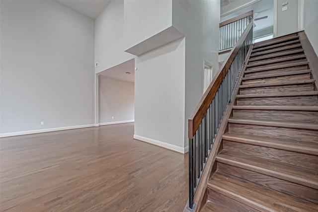 stairway with wood finished floors, a towering ceiling, and baseboards