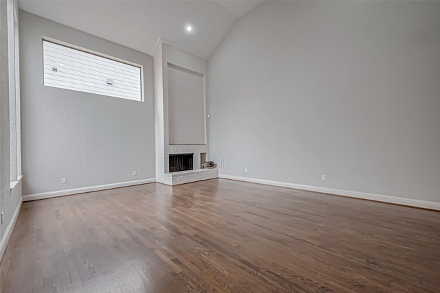 unfurnished living room featuring lofted ceiling, a brick fireplace, baseboards, and wood finished floors