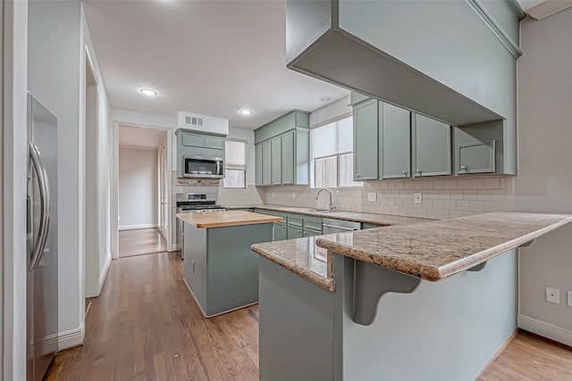 kitchen with a breakfast bar area, a peninsula, butcher block countertops, stainless steel appliances, and a kitchen island