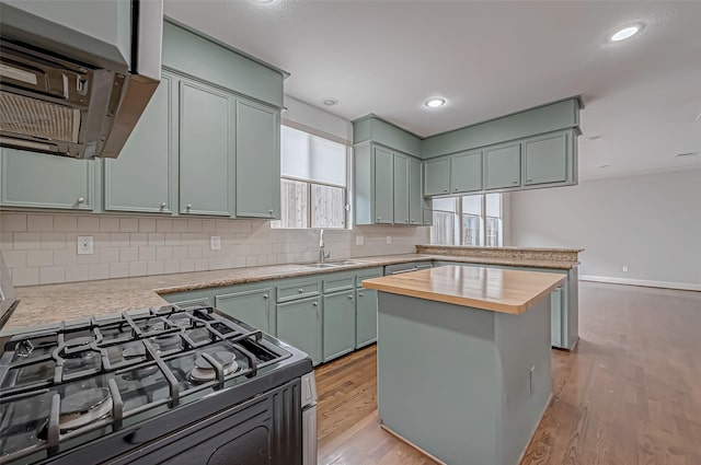 kitchen with light wood-style flooring, butcher block counters, a sink, range hood, and black gas range oven