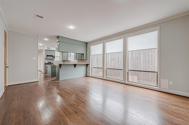 unfurnished living room featuring crown molding, wood finished floors, visible vents, and baseboards