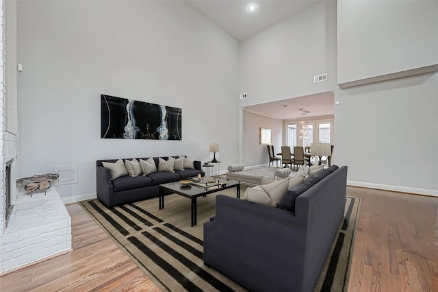 living room with a high ceiling, light wood-type flooring, visible vents, and baseboards