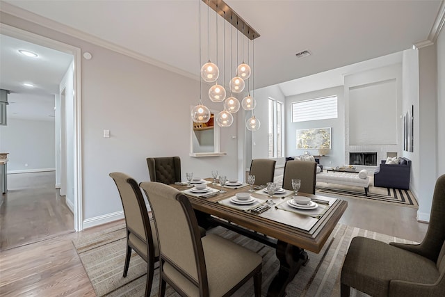 dining area featuring a brick fireplace, baseboards, visible vents, and wood finished floors