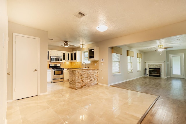 kitchen featuring light countertops, appliances with stainless steel finishes, glass insert cabinets, open floor plan, and white cabinets