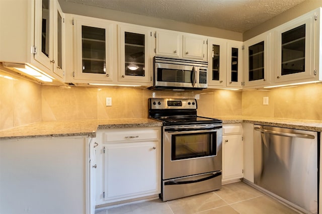 kitchen featuring appliances with stainless steel finishes, glass insert cabinets, and white cabinets