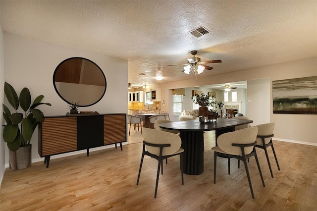 dining space with a textured ceiling, light wood-type flooring, visible vents, and baseboards