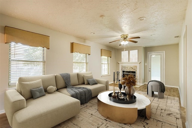 living area featuring a ceiling fan, a fireplace, a textured ceiling, and baseboards