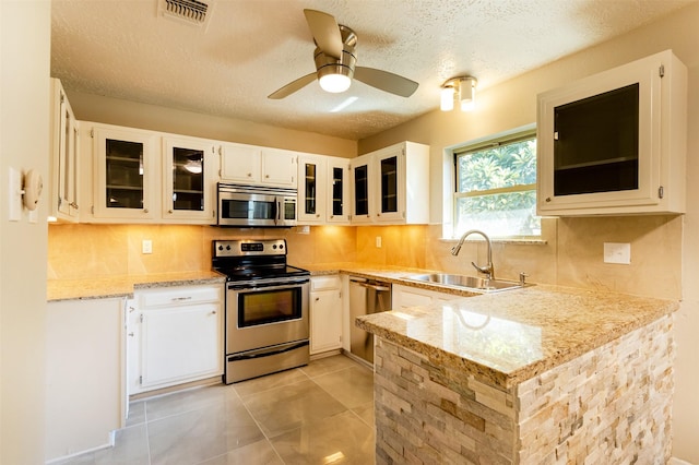 kitchen with appliances with stainless steel finishes, white cabinets, glass insert cabinets, and a sink