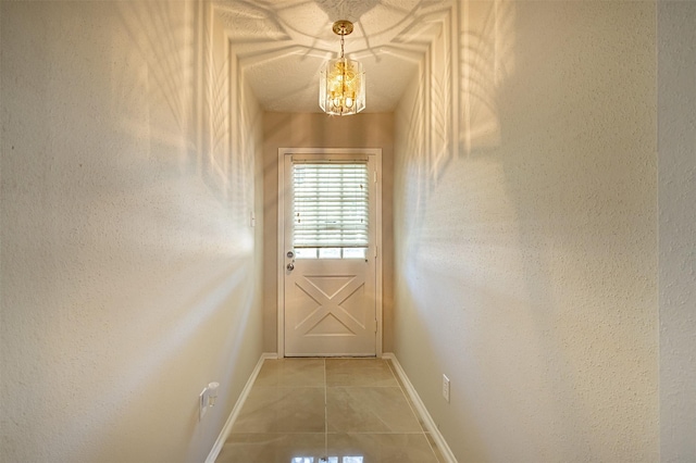 doorway with a chandelier, a textured wall, baseboards, and tile patterned floors