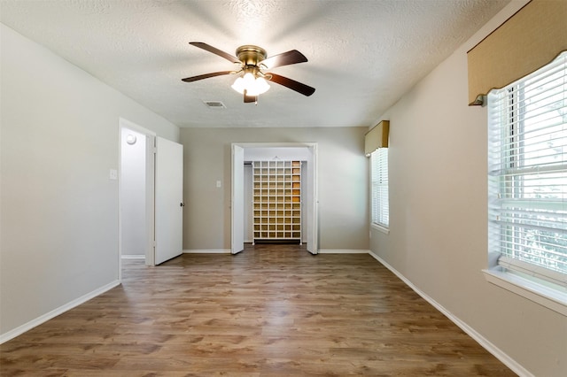 empty room featuring a ceiling fan, visible vents, a textured ceiling, and wood finished floors