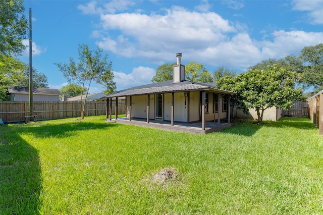 rear view of property with a patio, a chimney, a lawn, metal roof, and a fenced backyard