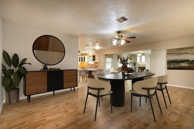 dining space with light wood finished floors, visible vents, a textured ceiling, and baseboards