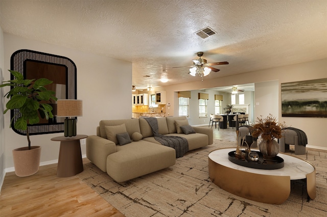 living room with visible vents, baseboards, light wood-style floors, and a textured ceiling