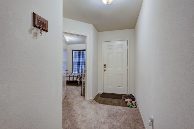 hallway with light colored carpet, a textured wall, and baseboards