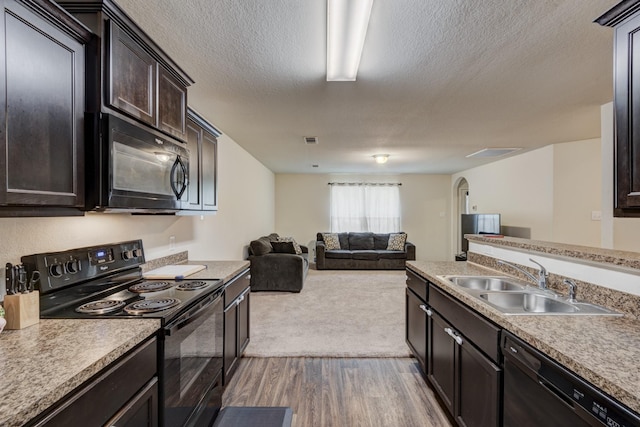 kitchen featuring light countertops, open floor plan, a sink, dark brown cabinets, and black appliances