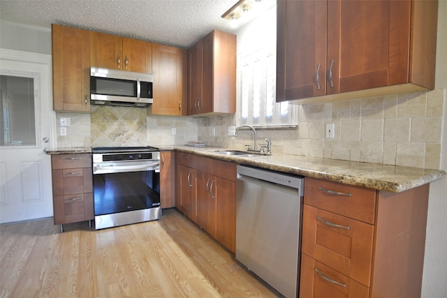 kitchen featuring a textured ceiling, decorative backsplash, light wood-style flooring, a sink, and appliances with stainless steel finishes