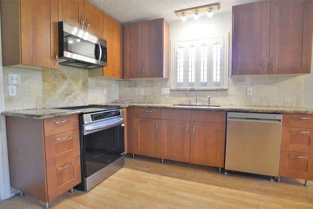 kitchen with a textured ceiling, a sink, appliances with stainless steel finishes, light wood-type flooring, and light stone countertops