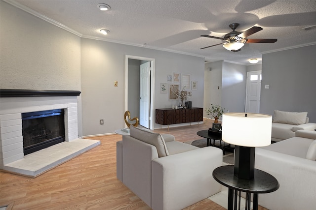 living room with light wood-style floors, a brick fireplace, ceiling fan, ornamental molding, and a textured ceiling
