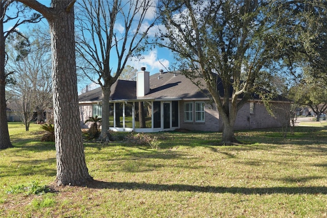 back of property with a sunroom, brick siding, a lawn, and a chimney