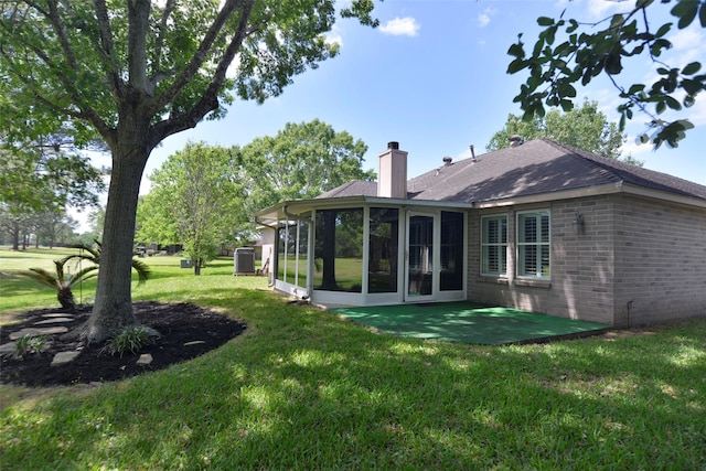 back of house with a sunroom, a yard, a chimney, cooling unit, and brick siding