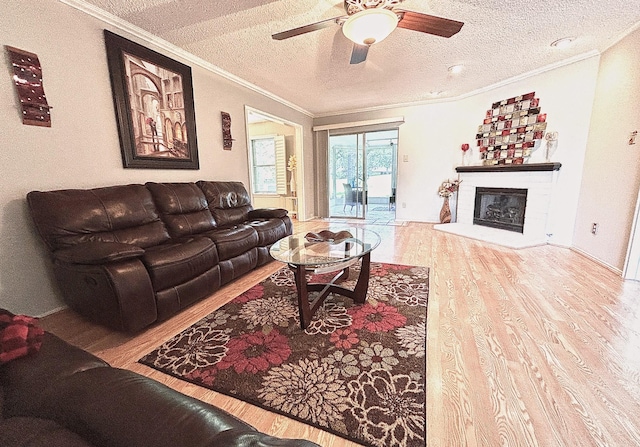 living room with a textured ceiling, a glass covered fireplace, ornamental molding, wood finished floors, and a ceiling fan