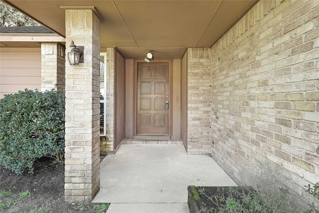 view of exterior entry with roof with shingles and brick siding