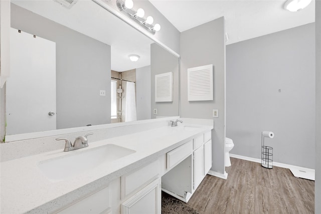 bathroom featuring double vanity, baseboards, toilet, wood finished floors, and a sink