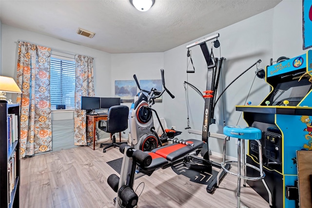 exercise area featuring a textured ceiling, wood finished floors, and visible vents