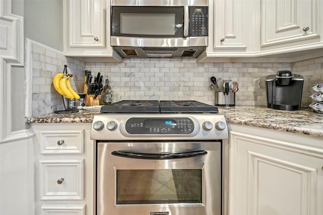 kitchen featuring stainless steel appliances, light stone countertops, white cabinets, and decorative backsplash