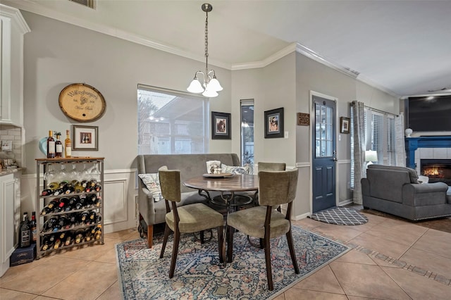 dining room with ornamental molding, a tile fireplace, a chandelier, and light tile patterned flooring