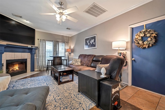 living room featuring a tile fireplace, visible vents, crown molding, and light tile patterned flooring