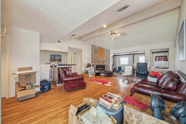 living room featuring vaulted ceiling with beams, a fireplace, visible vents, light wood-style floors, and a textured ceiling