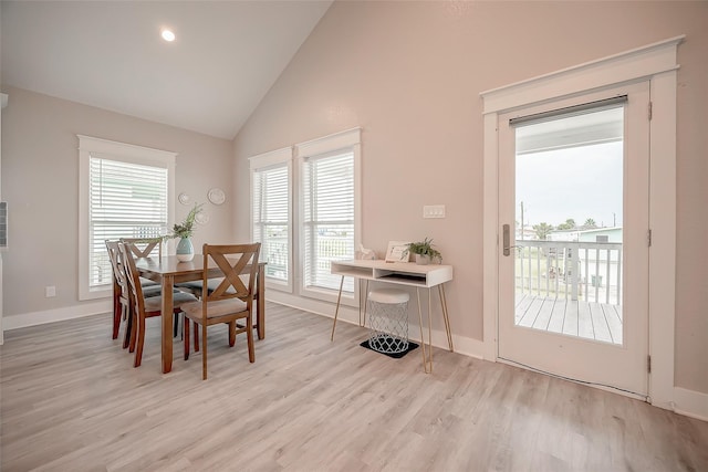 dining space with light wood-style floors, high vaulted ceiling, and baseboards