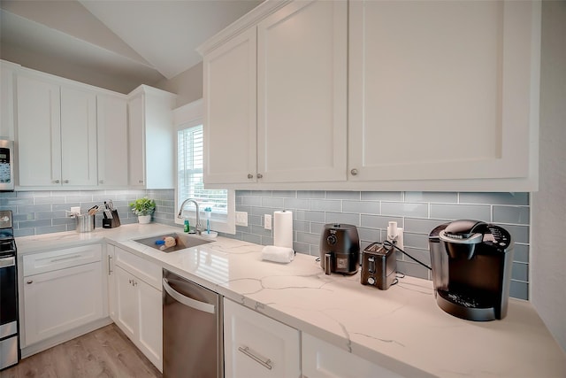 kitchen with stainless steel appliances, white cabinetry, vaulted ceiling, a sink, and light stone countertops