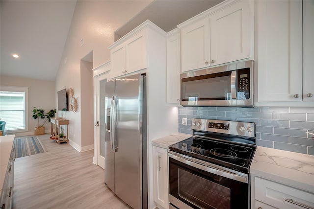 kitchen featuring light stone counters, white cabinetry, vaulted ceiling, appliances with stainless steel finishes, and decorative backsplash