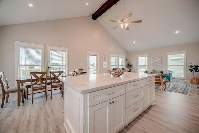 kitchen with light stone counters, white cabinets, open floor plan, a center island, and plenty of natural light