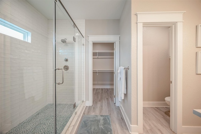 full bathroom with toilet, wood finished floors, baseboards, a spacious closet, and a stall shower