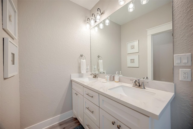 full bathroom featuring a textured wall, double vanity, a sink, and baseboards