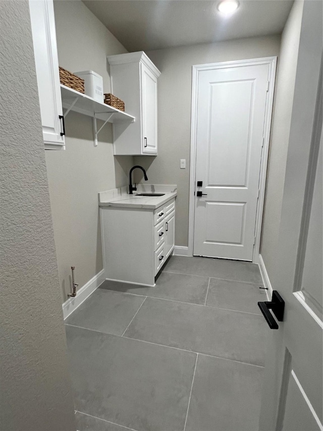 washroom with light tile patterned floors, a sink, and baseboards