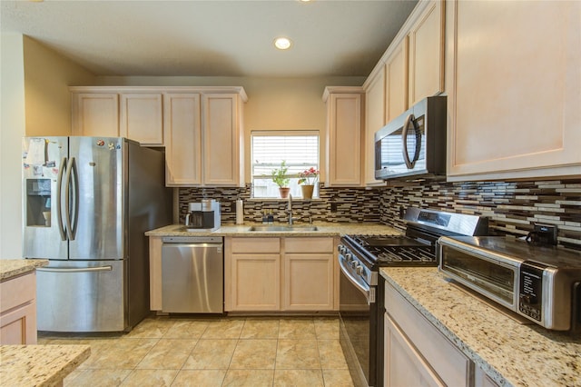 kitchen featuring a toaster, backsplash, appliances with stainless steel finishes, a sink, and light stone countertops