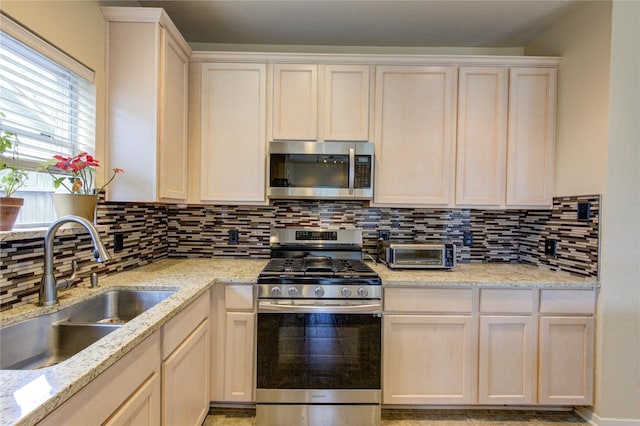 kitchen featuring stainless steel appliances, light stone counters, a sink, and tasteful backsplash