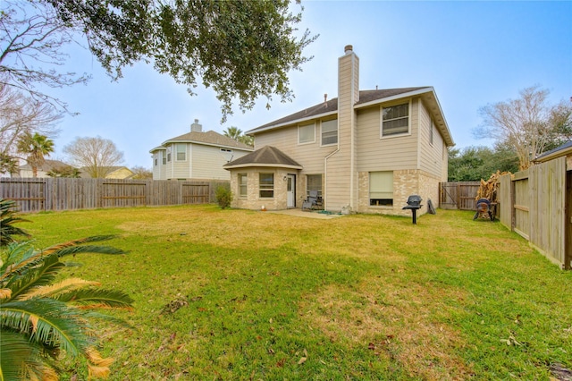 rear view of house with a fenced backyard, a lawn, a chimney, and a patio