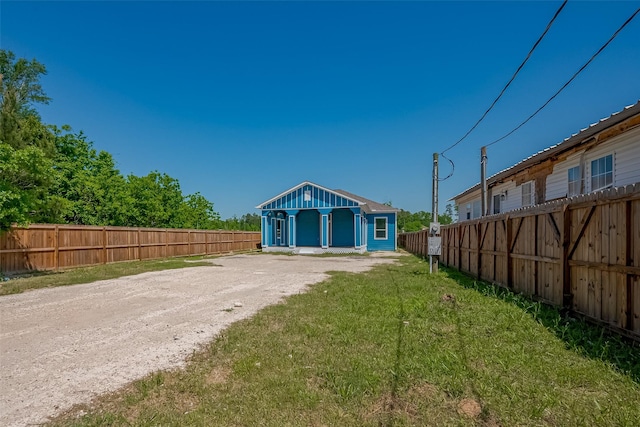 rear view of house with a fenced backyard, an outdoor structure, a lawn, and dirt driveway