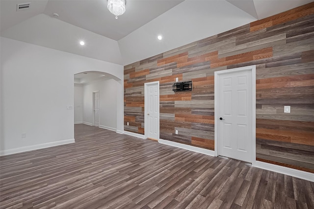 unfurnished room with arched walkways, wood finished floors, wooden walls, and visible vents