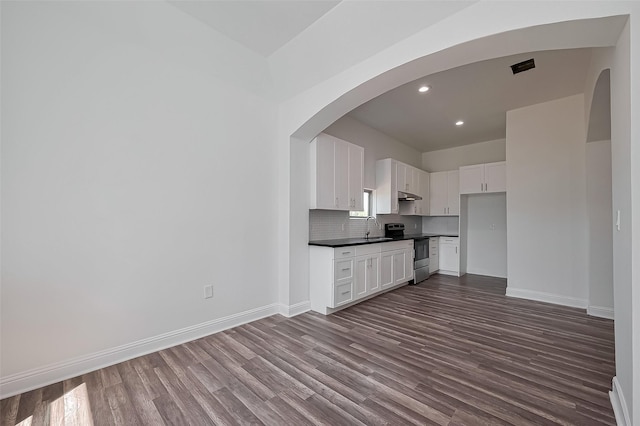 kitchen featuring stainless steel range with electric stovetop, under cabinet range hood, dark wood-style flooring, a sink, and dark countertops