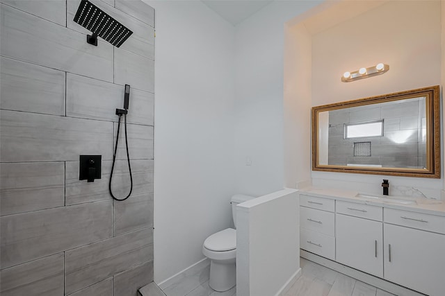 full bathroom featuring toilet, a tile shower, vanity, and baseboards