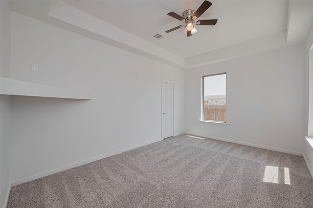 carpeted empty room featuring visible vents, baseboards, a ceiling fan, and a raised ceiling